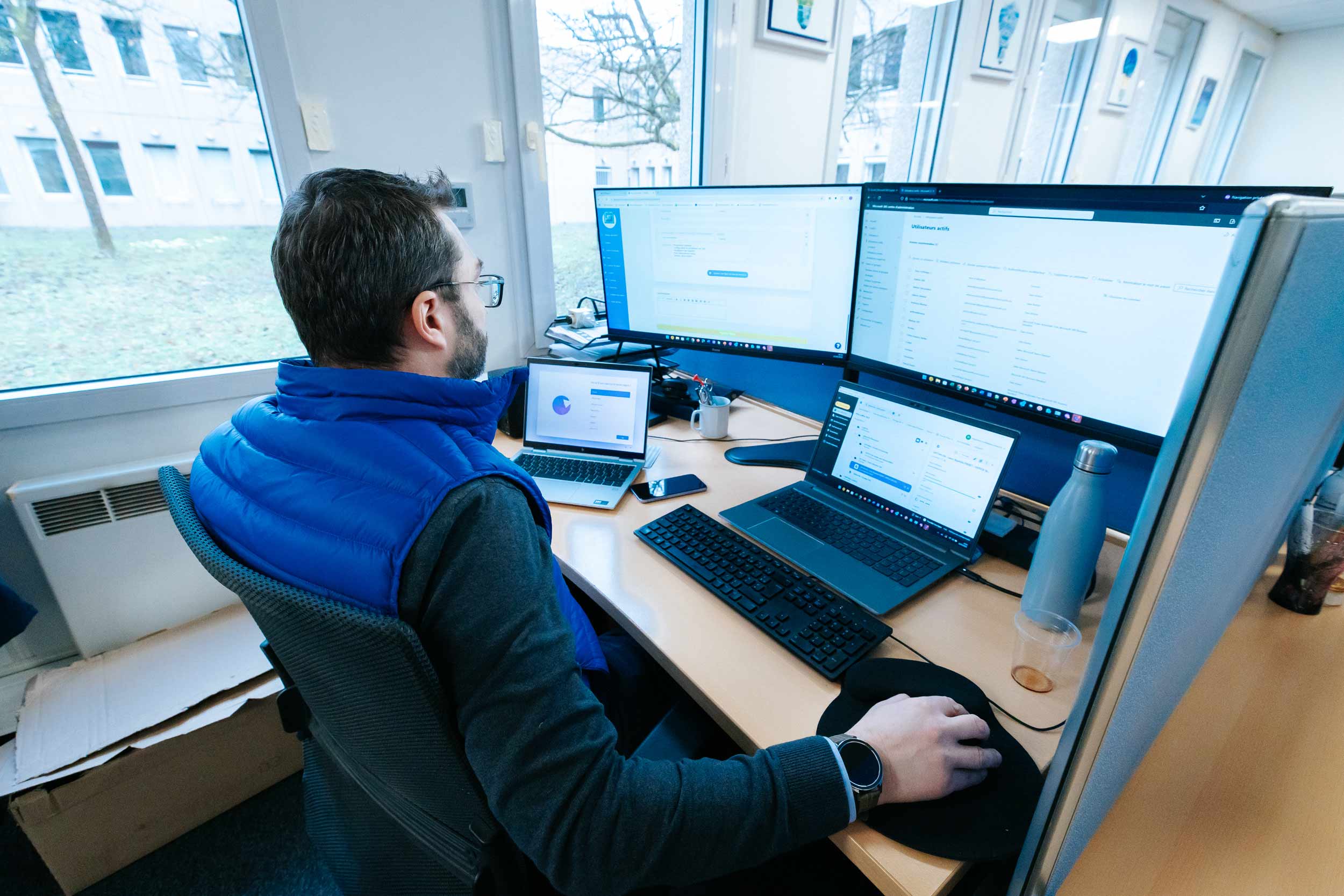 Photo d'un informaticiens entrain de travailler sur plusieurs ordinateurs